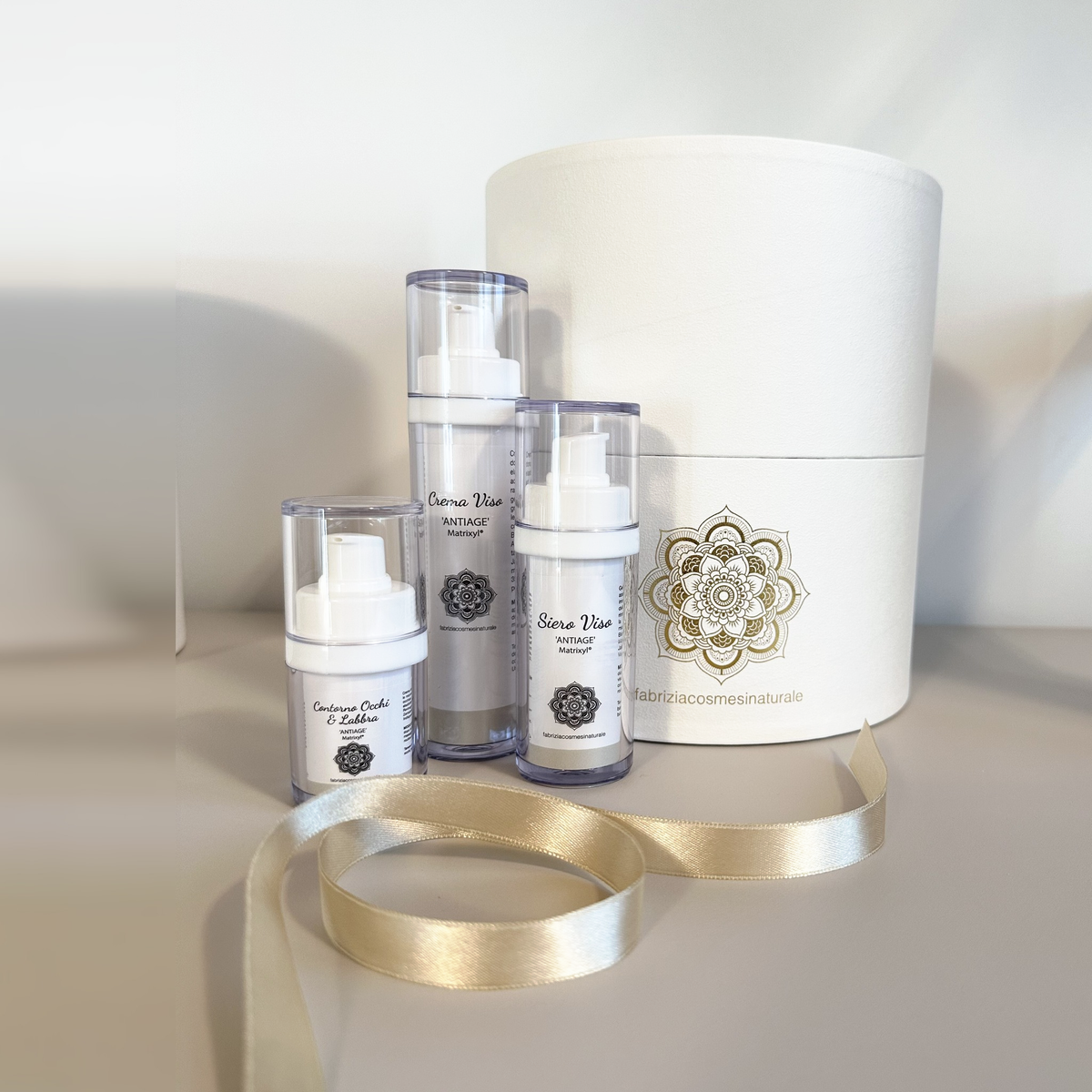 Box regalo con tre cosmetici viso e nastro in raso oro: esempio di composizione, i cosmetici non sono compresi